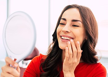 Woman in red shirt admiring her smile in handheld mirror