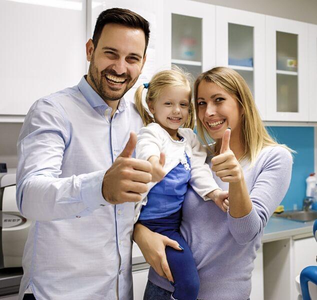 Smiling family of three giving thumbs up in dental office