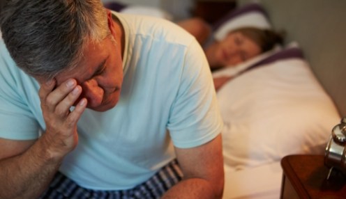 Man sitting on bed rubbing his eyes next to sleeping wife