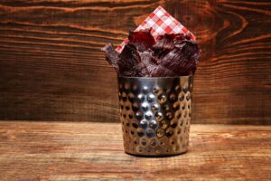 A tin full of beef jerky and a checkered napkin